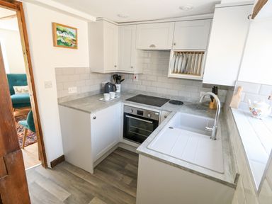 A kitchen with grey countertops white cabinets a built in oven electric cooktop and a white sink at Tiddlers Cottage in Uploders near Bridport