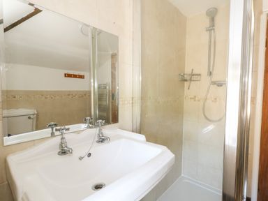 A bathroom with a white sink and two taps a large mirror a shower with a detachable showerhead and tiled walls at Tiddlers Cottage in Uploders near Bridport