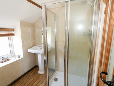 A bathroom with a glass shower enclosure a pedestal sink and a window with wooden blinds at Tiddlers Cottage in Uploders near Bridport