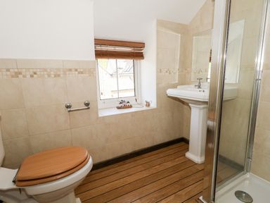 A bathroom with a toilet wooden seat a pedestal sink shower enclosure and window at Tiddlers Cottage in Uploders near Bridport