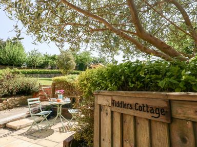 A small outdoor patio with a table set for breakfast and two chairs behind a wooden gate labelled Tiddlers Cottage in Uploders near Bridport