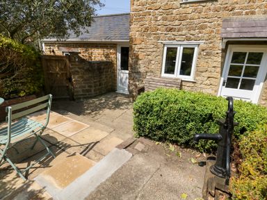 An outdoor patio area with a black water pump green chair stone walls and bushes at Tiddlers Cottage in Uploders near Bridport