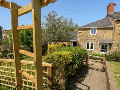 A stone house with a garden path wooden gate and green bushes at Tiddlers Cottage Uploders near Bridport