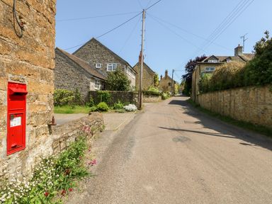 A village street with stone houses a red post box on a wall and plants along the roadside at Tiddlers Cottage in Uploders near Bridport
