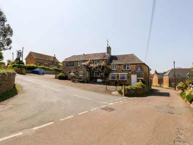A stone building with Crown Inn signs at a road junction with houses and a car nearby at Tiddlers Cottage in Uploders near Bridport