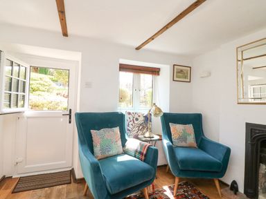 A sitting area with two blue armchairs next to a small window and door at Tiddlers Cottage in Uploders near Bridport