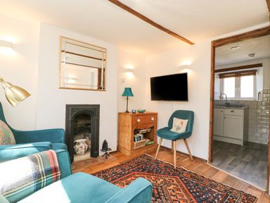 A sitting room with teal armchairs a wooden cabinet a fireplace and a wall mounted television at Tiddlers Cottage in Uploders near Bridport