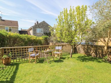 A garden with two chairs and a table on grass surrounded by trees and houses in the background at Tiddlers Cottage in Uploders near Bridport