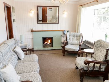 A sitting room with a fireplace three armchairs a sofa and a window at Sea Watch House in Roundstone County Galway