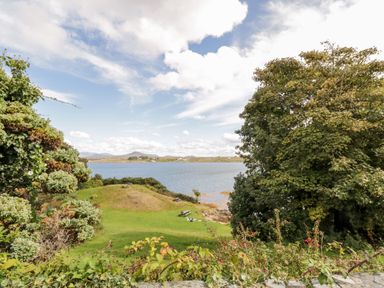 A grassy area with picnic tables near a body of water surrounded by trees at Sea Watch House in Roundstone County Galway