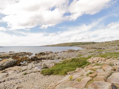 A rocky coastline with patches of grass under a partly cloudy sky at Sea Watch House in Roundstone County Galway