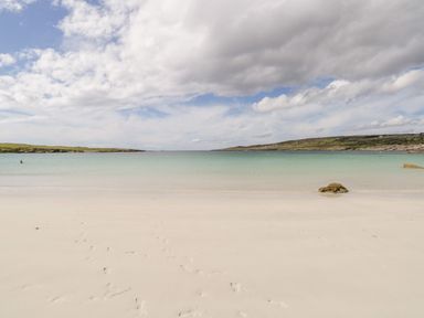 A beach with white sand and footprints leading to clear water at Sea Watch House in Roundstone County Galway