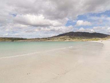 A sandy beach with turquoise water and a rocky hill under a cloudy sky at Sea Watch House in Roundstone County Galway