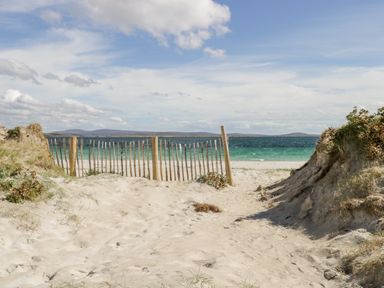 A sandy beach path with a wooden fence leading to the ocean and hills in the distance at Sea Watch House in Roundstone County Galway