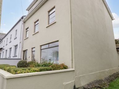 Exterior view of a two-story cream colored house with windows and garden at Sea Watch House in Roundstone County Galway