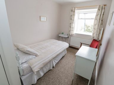 A small bedroom with a single bed a white desk a red chair a window with curtains and a wall-mounted sink at Sea Watch House in Roundstone County Galway