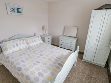 A bedroom with a bed, nightstand with lamp, dresser with mirror, wardrobe, and framed pictures on the wall at Sea Watch House in Roundstone County Galway