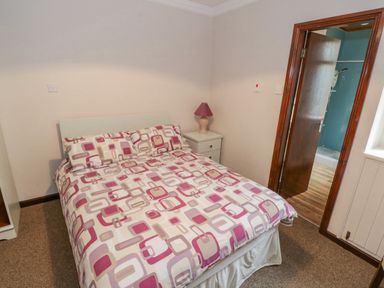 A bedroom with a patterned bedspread a bedside table with a lamp and an open door revealing a bathroom at Sea Watch House Roundstone County Galway