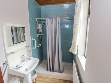 A small bathroom with a sink mirror shower with curtain and blue tiled walls at Sea Watch House in Roundstone County Galway