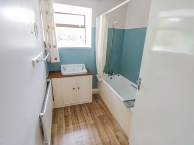 A bathroom with a bathtub shower combination blue tiled walls a sink cabinet wood floor and a radiator at Sea Watch House in Roundstone County Galway