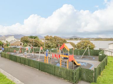 A fenced playground with slides and swings near a body of water and houses in Roundstone County Galway