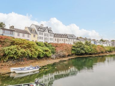 A row of houses behind shrubs by a calm water body with a small boat at Sea Watch House in Roundstone County Galway