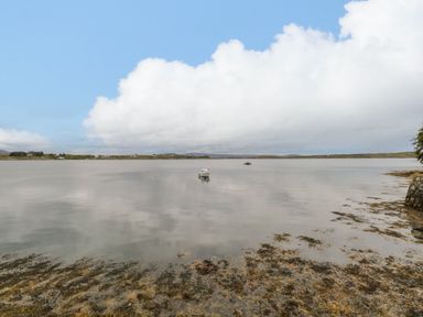 A calm body of water with two boats and a rocky shoreline at Sea Watch House in Roundstone County Galway