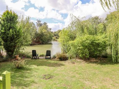 A garden with two black chairs facing a lake surrounded by trees at Lakeside Lodge Retreat in Tattershall