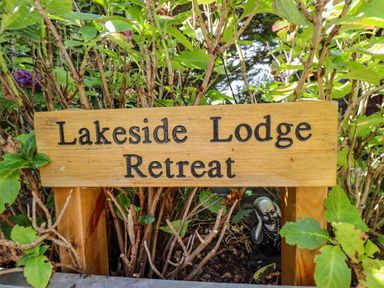 A wooden sign with Lakeside Lodge Retreat surrounded by green plants and shrubs in a garden