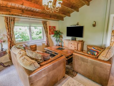 A living room with leather sofas wooden coffee table mounted TV and a window with curtains at Lakeside Lodge Retreat in Tattershall