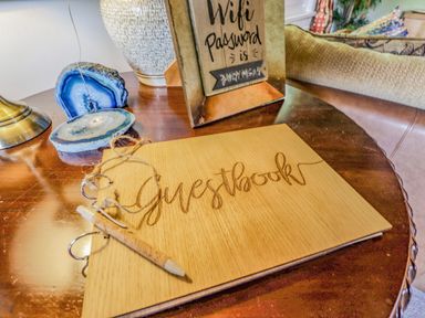 A wooden guestbook with a pencil on a wooden table next to a lamp and a framed wifi password sign at Lakeside Lodge Retreat in Tattershall