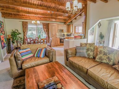 A living room with leather sofas and pillows a wooden coffee table with remotes a dining area and kitchen with wooden cabinets at Lakeside Lodge Retreat in Tattershall