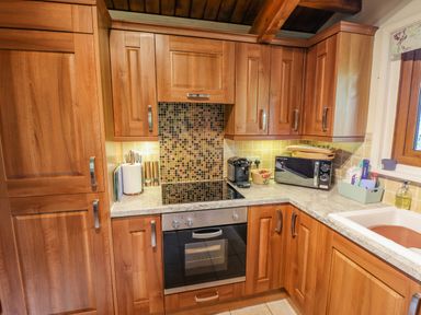 A kitchen with wooden cabinets a built in oven a microwave a coffee machine and a sink at Lakeside Lodge Retreat in Tattershall