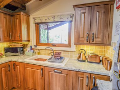 A kitchen with wooden cabinets a sink a microwave kettle toaster and canisters at Lakeside Lodge Retreat in Tattershall