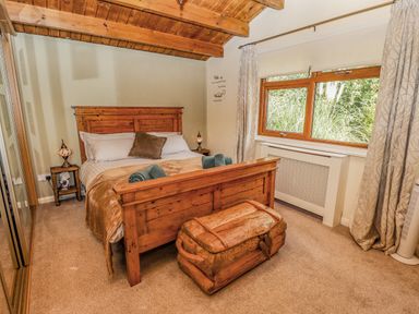 A bedroom with a wooden bed frame and chest near a window with curtains at Lakeside Lodge Retreat in Tattershall