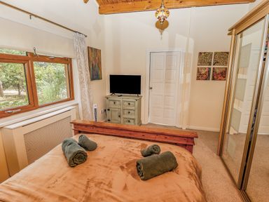 A bedroom with a bed with rolled towels a window a television on a cabinet and mirrored wardrobes at Lakeside Lodge Retreat in Tattershall