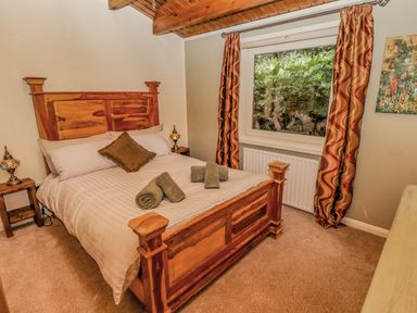 A bedroom with a wooden bed frame rolled towels on the bed patterned curtains and a window showing greenery at Lakeside Lodge Retreat in Tattershall