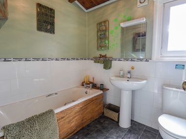 A bathroom with a bathtub partially covered with wood paneling a pedestal sink a toilet and a window at Lakeside Lodge Retreat in Tattershall