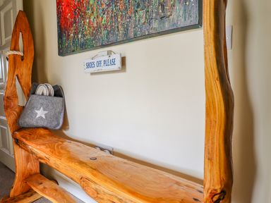 A wooden bench with a grey bag and slippers underneath a painting and a shoes off please sign at Lakeside Lodge Retreat in Tattershall