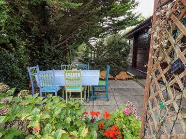 An outdoor patio with a table covered with a cloth and six chairs surrounded by greenery and flowers at Lakeside Lodge Retreat in Tattershall