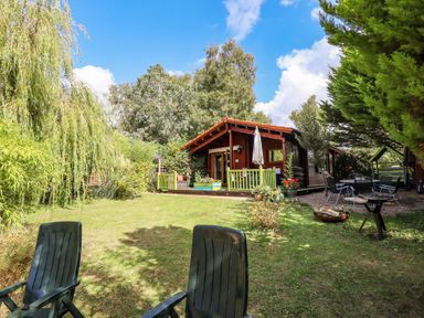A garden with chairs barbecue and a wooden cabin surrounded by trees at Lakeside Lodge Retreat in Tattershall