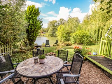 An outdoor patio with a round table and four chairs next to a garden with plants and a pond at Lakeside Lodge Retreat in Tattershall
