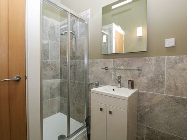 A bathroom with a shower enclosure, a sink with a cabinet, a mirror, and a wooden door at Bottom Lodge in Penhow