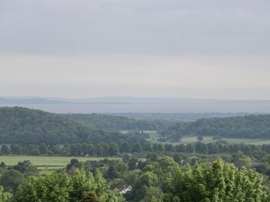A landscape view of green trees and fields with hills and a body of water in the distance at Bottom Lodge Penhow