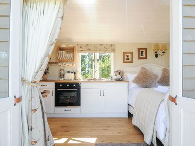 A small kitchen with white cabinets next to a bed with pillows and framed pictures on the wall at Orchard Retreat in East Worlington near Witheridge