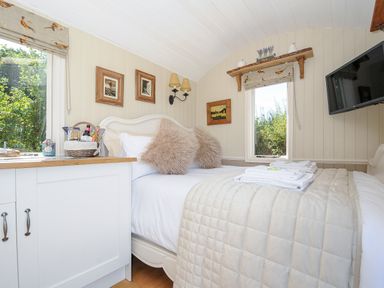 A bedroom with a bed with pillows and folded towels a TV mounted on the wall and a cabinet with a basket on top at Orchard Retreat in East Worlington near Witheridge