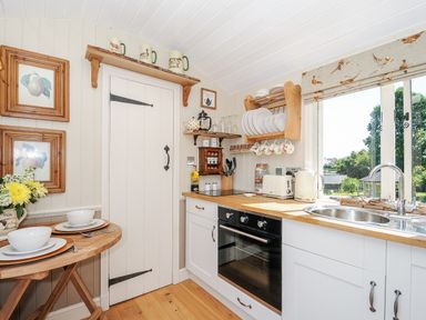 A kitchen with wooden countertops a white oven a sink near a window and a small dining table set for two at Orchard Retreat in East Worlington near Witheridge