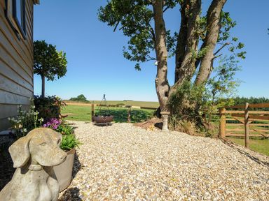 A gravel patio area with a dog statue trees a fire pit and wooden fence at Orchard Retreat in East Worlington near Witheridge
