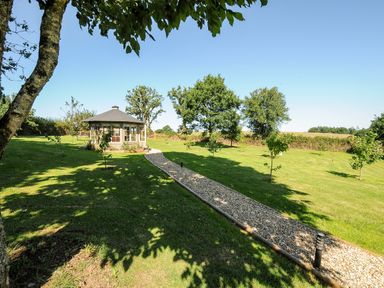 A garden area with a gravel path leading to a gazebo and young trees at Orchard Retreat in East Worlington near Witheridge