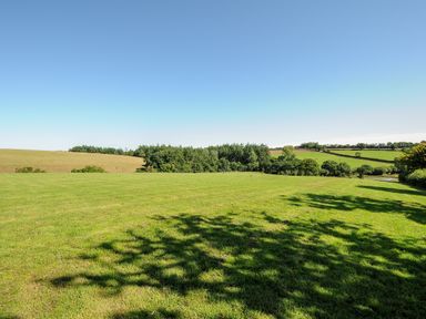 A large grassy field with hills trees and a clear sky at Orchard Retreat in East Worlington near Witheridge